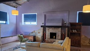 Una sala de estar con chimenea, un sofá, una estantería y dos lámparas colgantes.