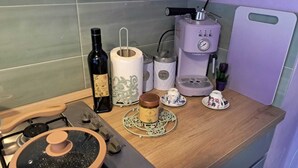 Una encimera de cocina con una estufa a gas, una cafetera, una botella de vino, un rollo de toallas de papel y una pequeña planta en maceta.