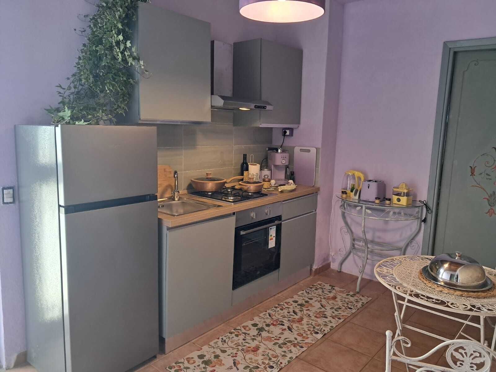 A compact kitchen with a refrigerator, stove, sink, and oven. There is a small table with a decorative cover and a potted plant.