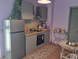 Cocina compacta con refrigerador, estufa, pileta y horno. Hay una mesita con un mantel decorativo y una planta en maceta.