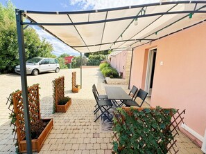 A covered patio area with a table and chairs, wooden planters with greenery, and a car parked outside. - Luxury Villa with Spa, Sauna, and Billiards Table (Montauroux)