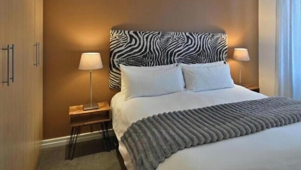 A hotel room with a zebra-patterned headboard, a bed with white linens, two bedside lamps, and a window with curtains. - Entire 2bdr Aparthotel With Kitchen & Dining (Cape Town)