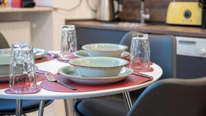 A dining table set with plates, glasses, and cutlery, with a kitchen area in the background. - Lit Living Weinheim (Weinheim)