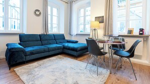 A living room with a blue sectional sofa, a dining table with chairs, a lamp, and a radiator. - Lit Living Weinheim (Weinheim)