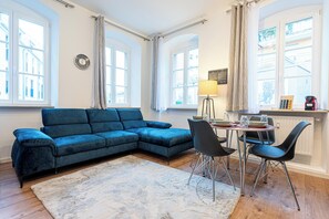 Ein Wohnzimmer mit einem blauen Ecksofa, einem Esstisch mit Stühlen, einer Lampe und einer Heizung.