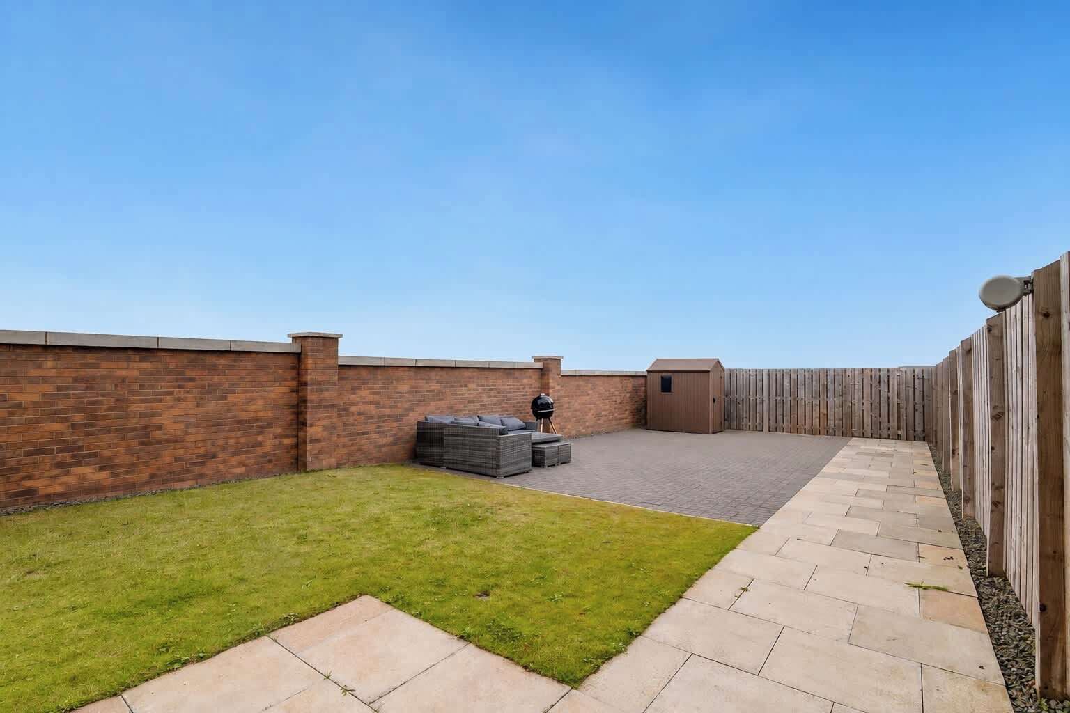 A backyard with a brick wall, a wooden fence, a barbecue grill, a shed, and a grassy area.