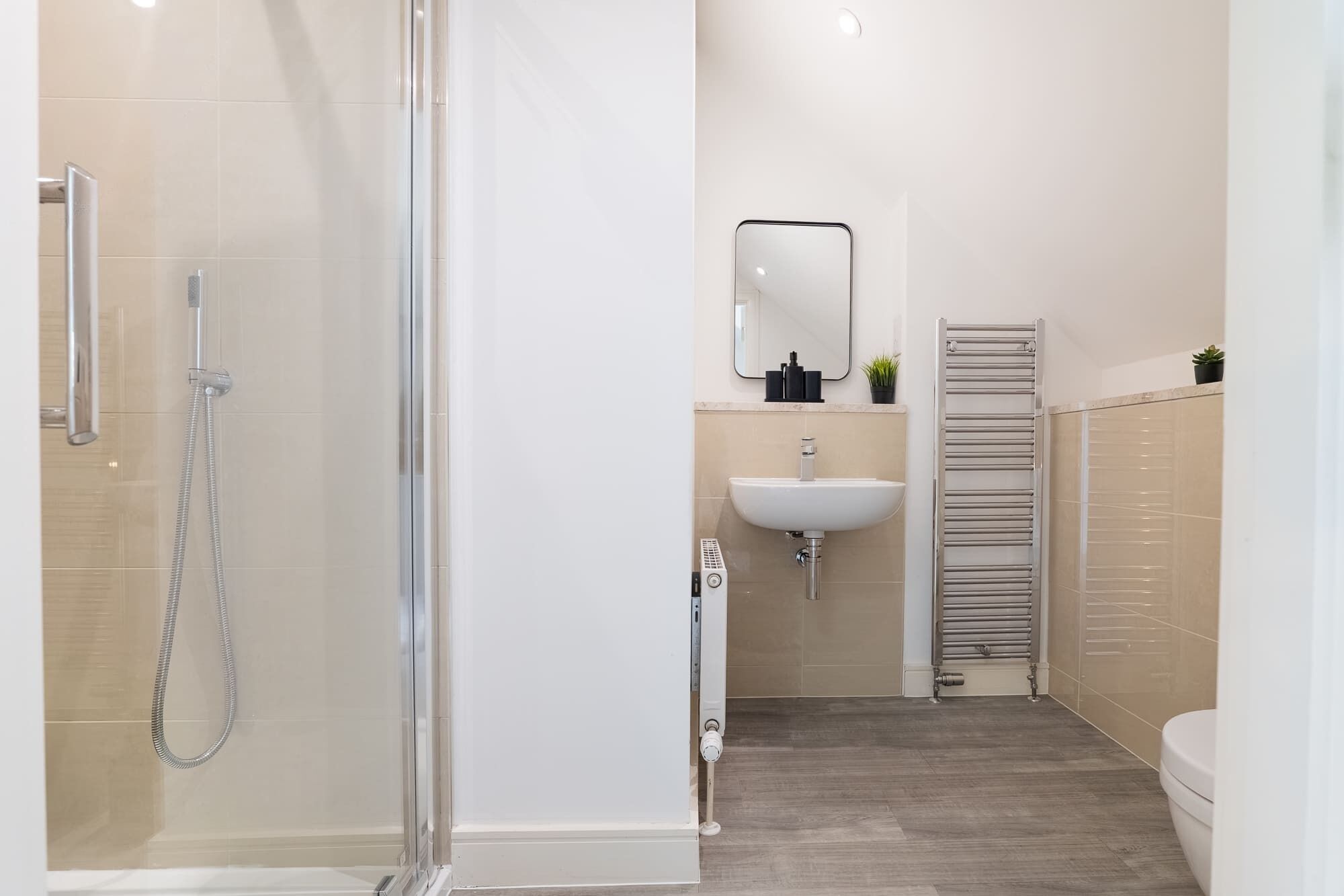 A modern bathroom with a glass shower enclosure, a white sink, and a towel rack.