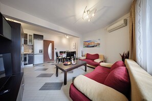 Ein modernes Wohnzimmer mit Fernseher, Sofa, Esstisch und einer Küche im Hintergrund.