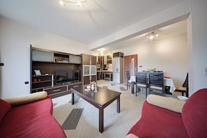 Ein modernes Wohnzimmer mit Fernseher, Sofa, Esstisch und Küchenzeile.