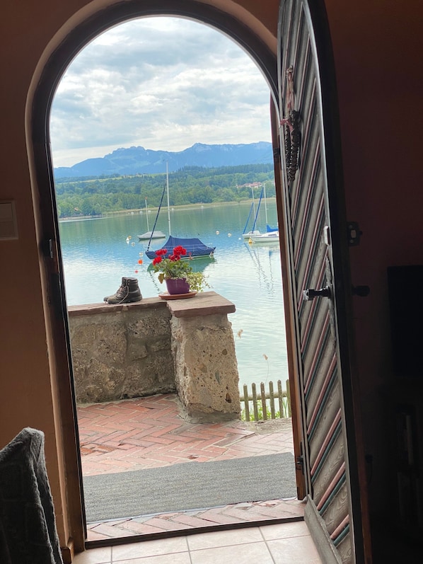 Eine geöffnete Tür, die auf einen Balkon mit Blick auf einen See, Boote und Berge führt.