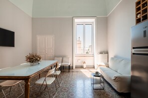 Una cocina moderna con refrigerador, una mesa de comedor con sillas, un sofá blanco y una ventana con vistas a edificios.