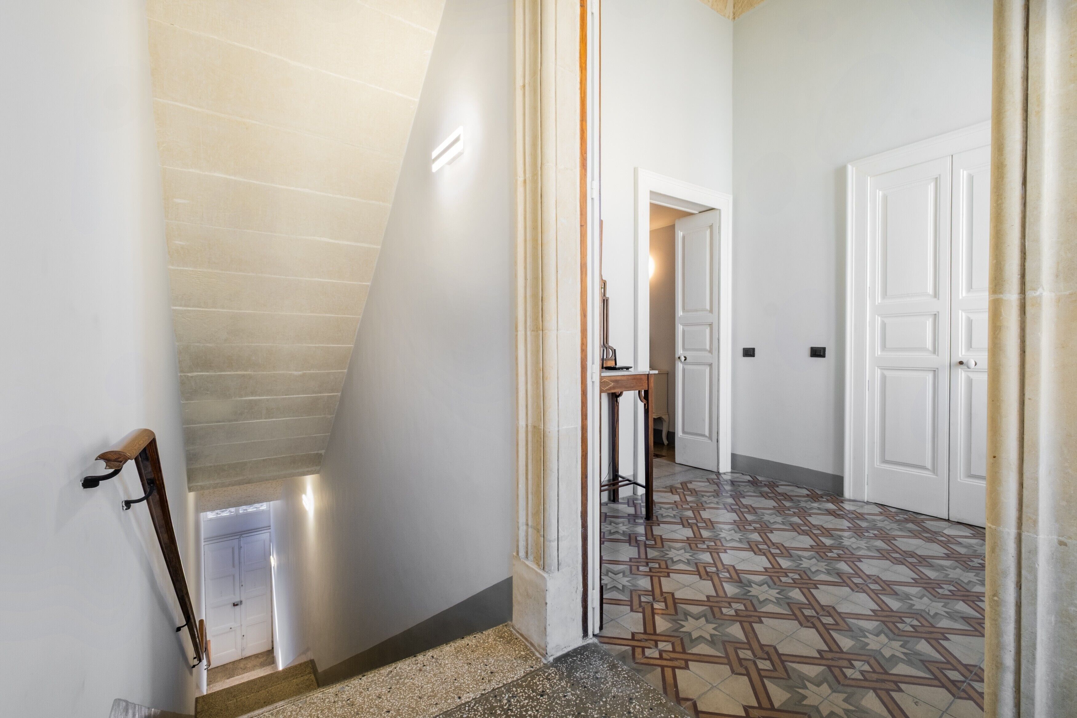 A hallway with a tiled floor, a staircase, and a door leading to another room.