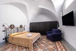 Ein Schlafzimmer mit einem Bett, einem blauen Sessel, einem Fernseher und einem gemusterten Boden.