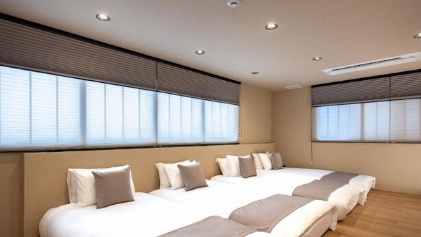Une chambre d’hôtel avec un grand lit, des luminaires au plafond et des fenêtres équipées de stores.