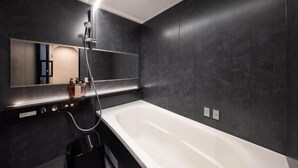 Une salle de bain moderne avec une grande baignoire blanche, une douchette à main et un miroir fixé au mur.