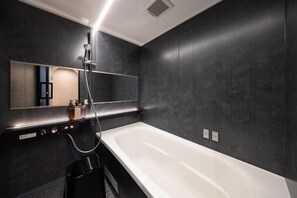 A modern bathroom with a large white bathtub, a handheld showerhead, and a wall-mounted mirror. - JAPAVISTA Morino-to (TENGACHAYA, NISHINARI WARD)