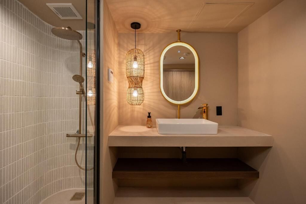 Un baño moderno con ducha de vidrio, un lavamanos blanco con grifo dorado y un espejo con marco dorado.
