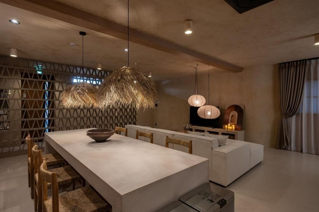 A modern dining area with a large table, chairs, and pendant lighting.