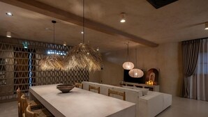 Un espace de salle à manger moderne, doté d’une grande table, de chaises et de luminaires suspendus.