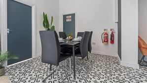 Een eethoek met een tafel gedekt voor vier personen, zwarte stoelen, een potplant en brandblussers aan de muur.
