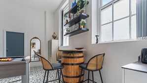 Een kamer met een pooltafel, twee barkrukken, een houten vat en een boekenplank met decoratieve objecten.