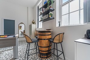 Ein Raum mit Poolbillard, zwei Barhocker, einem Holzfass und einem Bücherregal mit Dekoration.