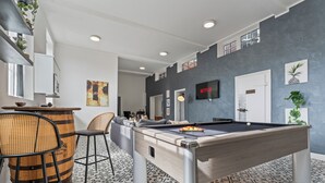 Een pooltafel in een ruimte met een patroon vloer, een bar met krukken, en een televisie aan de muur.