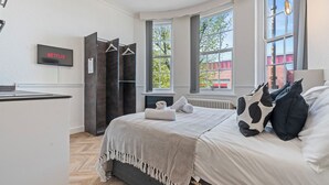 Een slaapkamer met een bed, een televisie waarop 'NETFLIX' staat, een radiator en een raam met uitzicht op bomen.