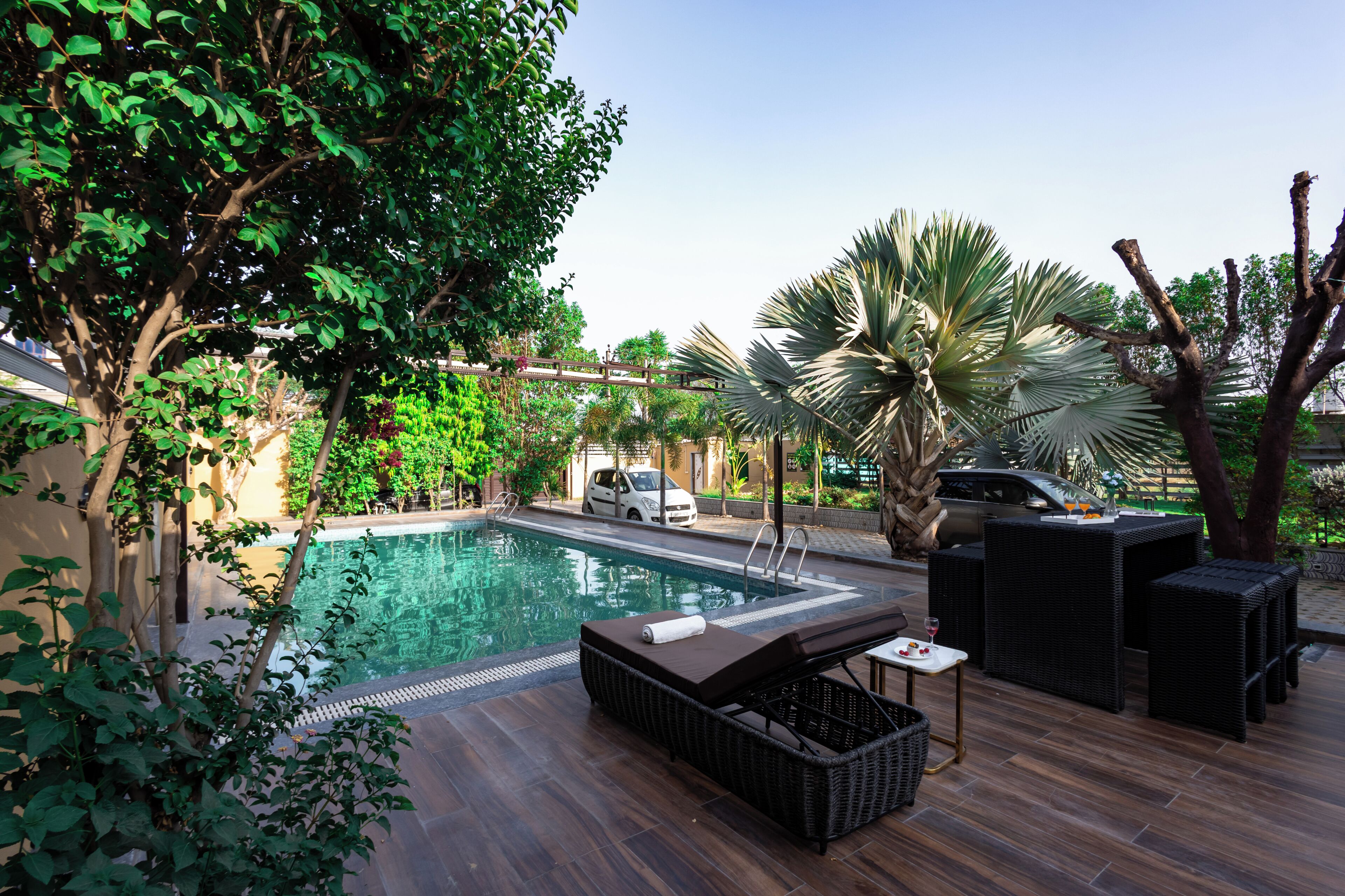 Uma piscina com espreguiçadeiras e uma mesa, rodeada por vegetação e árvores.