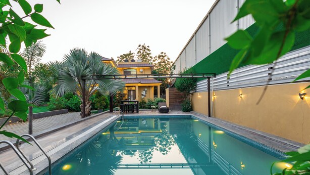 Ein Swimmingpool mit Terrassenbereich, umgeben von Grünflächen und einem Gebäude mit gelber Fassade.