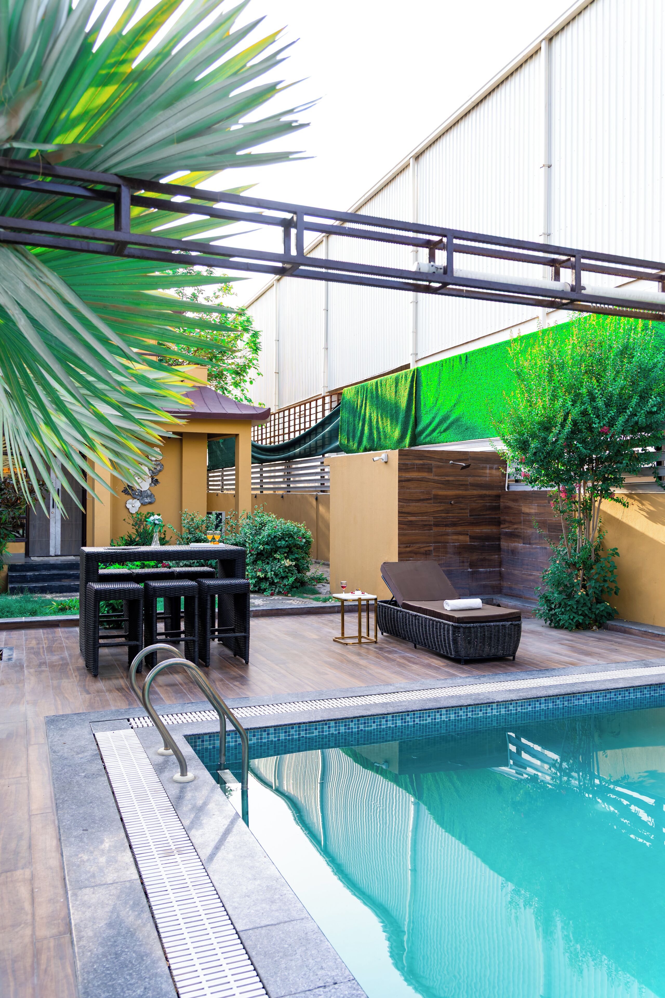 A swimming pool with a lounge area, a palm tree, and a building in the background.