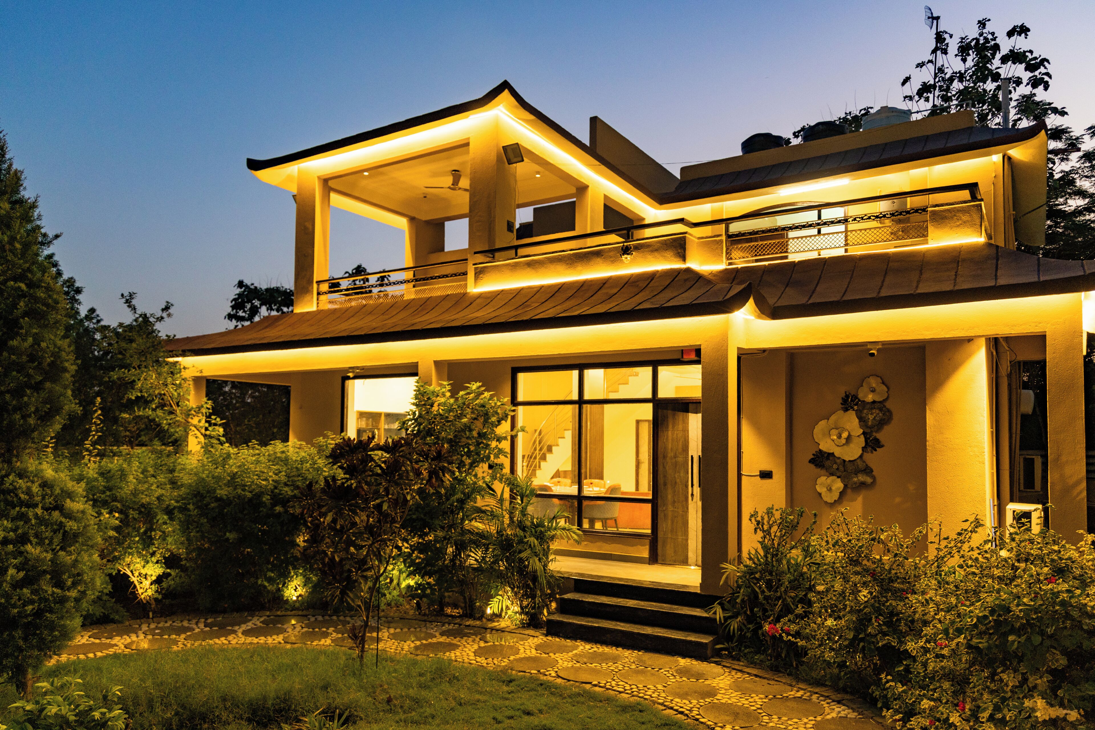 A modern two-story house with a balcony, large windows, and a well-maintained garden.