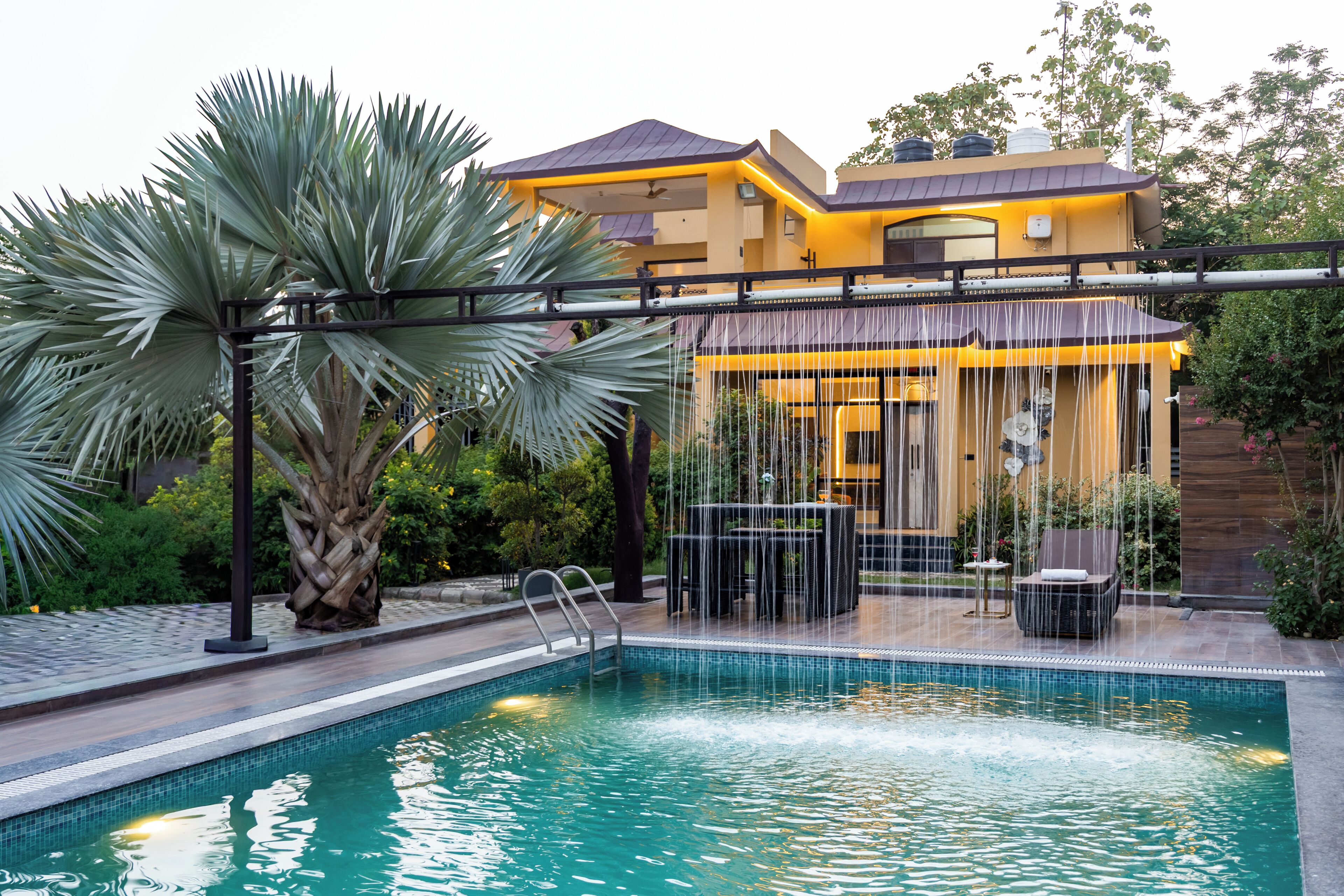 A swimming pool with a waterfall feature, a covered seating area, and a modern house in the background.