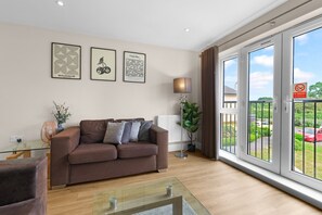 A modern living room with a brown sofa, glass coffee table, and framed artwork on the wall. - Heathrow Living 2BDR 2BA Apt by 360 Stays - Apt 11 (Stanwell)