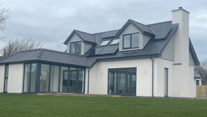 A modern two-story house with large glass windows, a sloped roof, and a chimney. - Ty Hebog (Beaumaris)