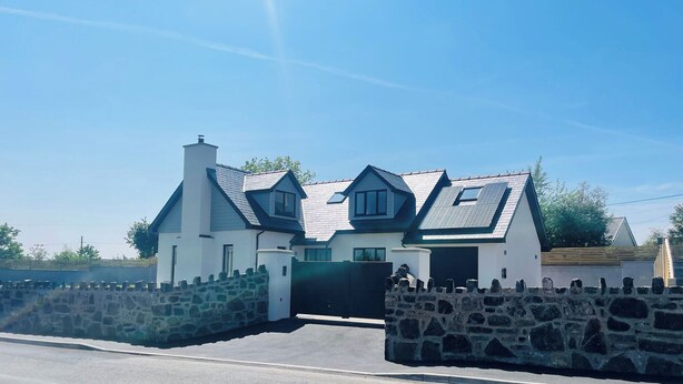 A modern house with a stone wall entrance, a garage, and a sloped roof. - Ty Hebog (Beaumaris)