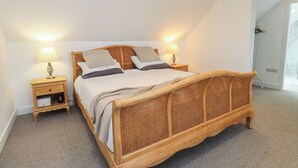 A bedroom with a wooden bed, two bedside tables, and a nightstand with a lamp. - Ty Hebog (Beaumaris)