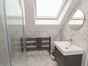 Ein modernes Badezimmer mit Dachfenster, einer Duschkabine aus Glas, einem Handtuchhalter, einem Waschbecken und Marmorböden.