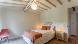 A bedroom with a bed, a chair, a bedside table with a lamp, and a woven rug. - Holiday Home "Mas des Amandiers" with Private Pool, Terrace, and Wi-Fi (Jonquières)