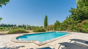A swimming pool with stone tiles, surrounded by greenery and a tall tree. - Holiday Home "Mas des Amandiers" with Private Pool, Terrace, and Wi-Fi (Jonquières)