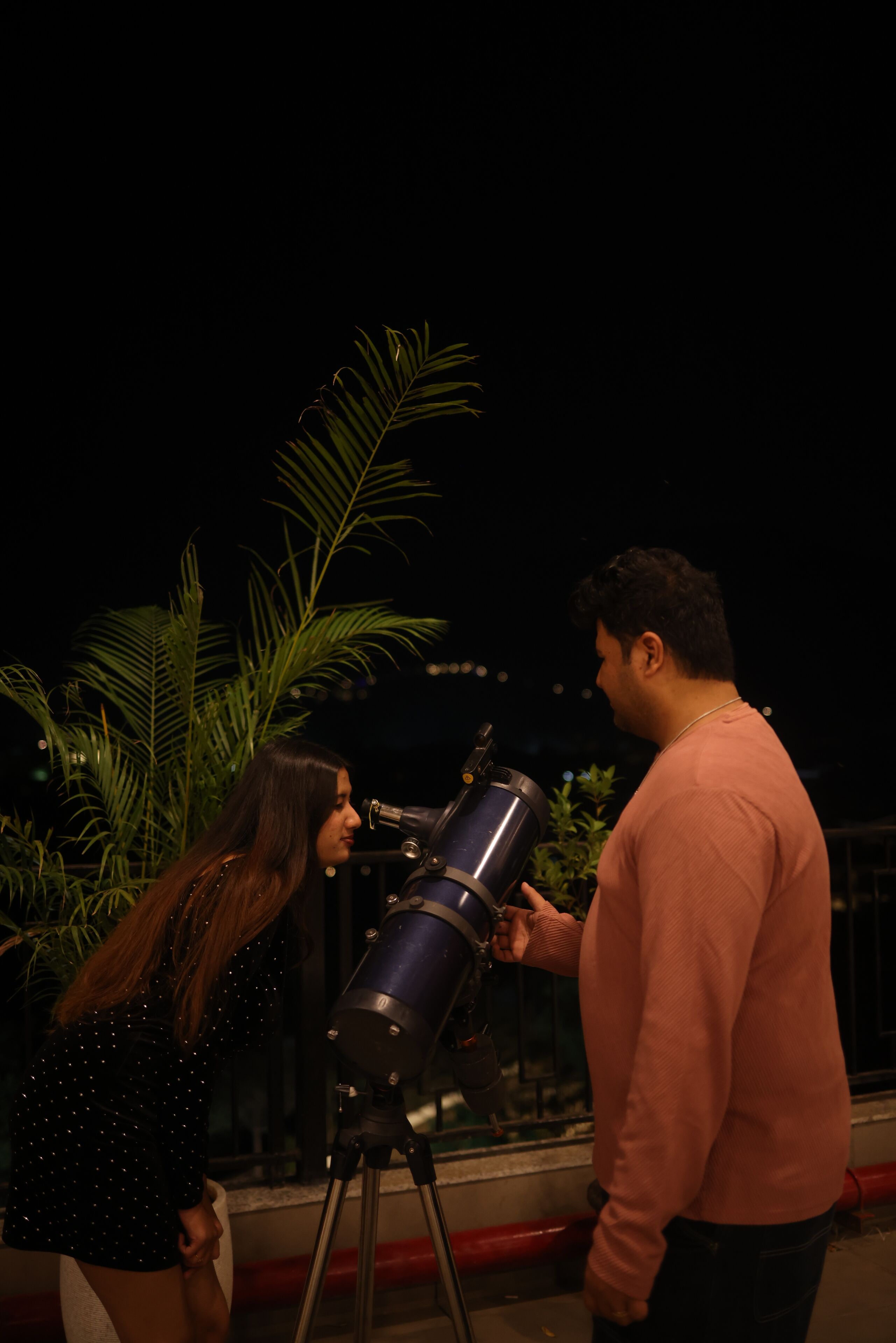 Two people using a telescope outdoors at night.
