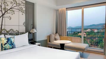 Habitación de hotel con cama, sofá, una mesita y un ventanal que ofrece vistas del paisaje.