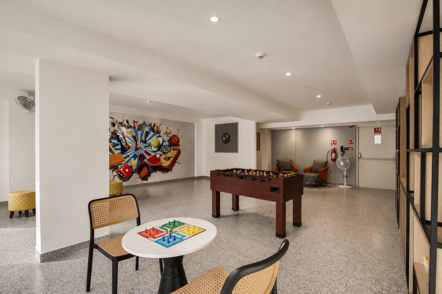 A room with a foosball table, a dartboard, and a colorful abstract mural on the wall.