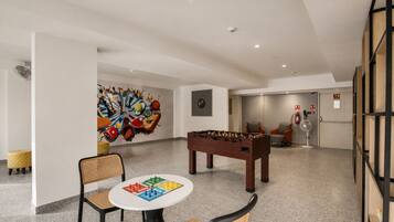 A room with a foosball table, a dartboard, and a colorful abstract mural on the wall.
