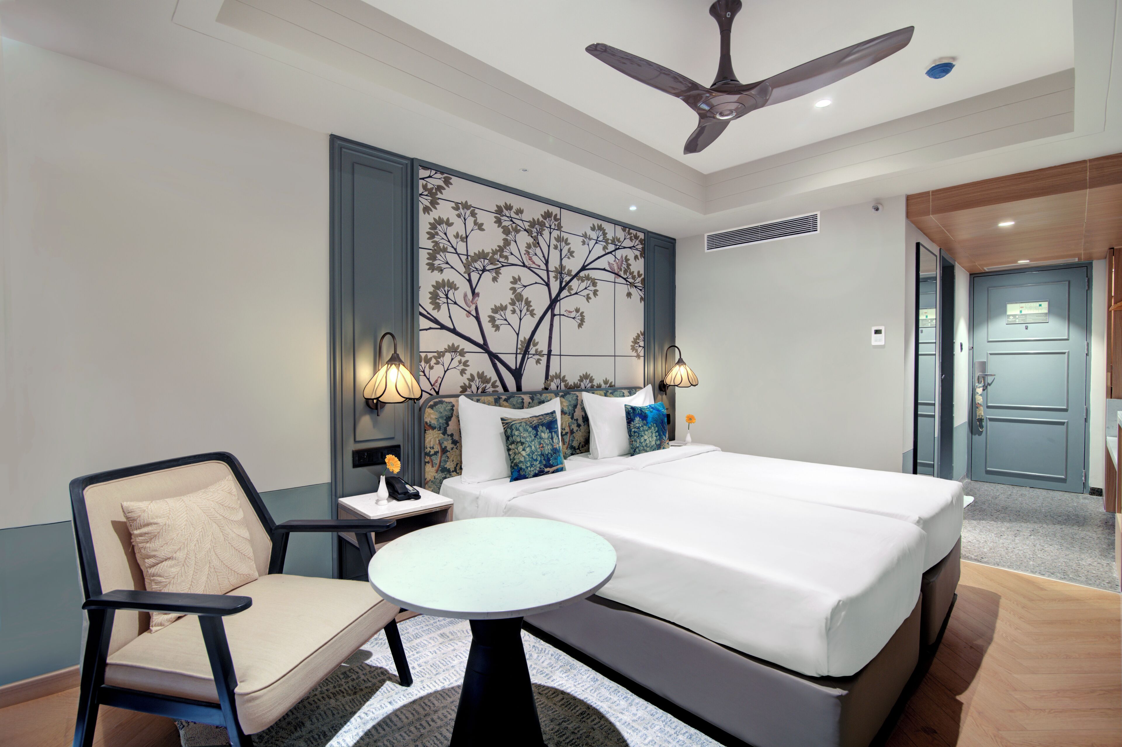 A hotel room with a bed, bedside table, chair, and a ceiling fan.