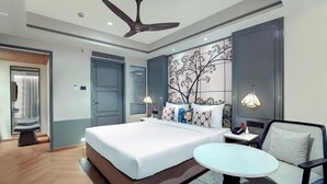Una habitación de hotel moderna con una cama grande, una mesita de noche con lámpara, una silla y un panel decorativo en la pared.