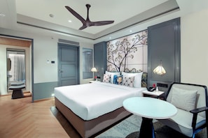 Una habitación de hotel moderna con una cama grande, una mesita de noche con lámpara, una silla y un panel decorativo en la pared.