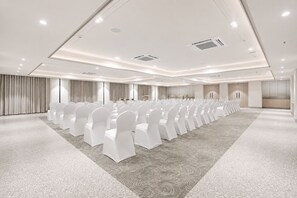 A conference room with rows of white chairs, a carpeted floor, and a modern ceiling design.