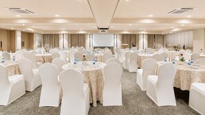 Un salón de conferencias con mesas redondas, sillas blancas y una pantalla para proyector.