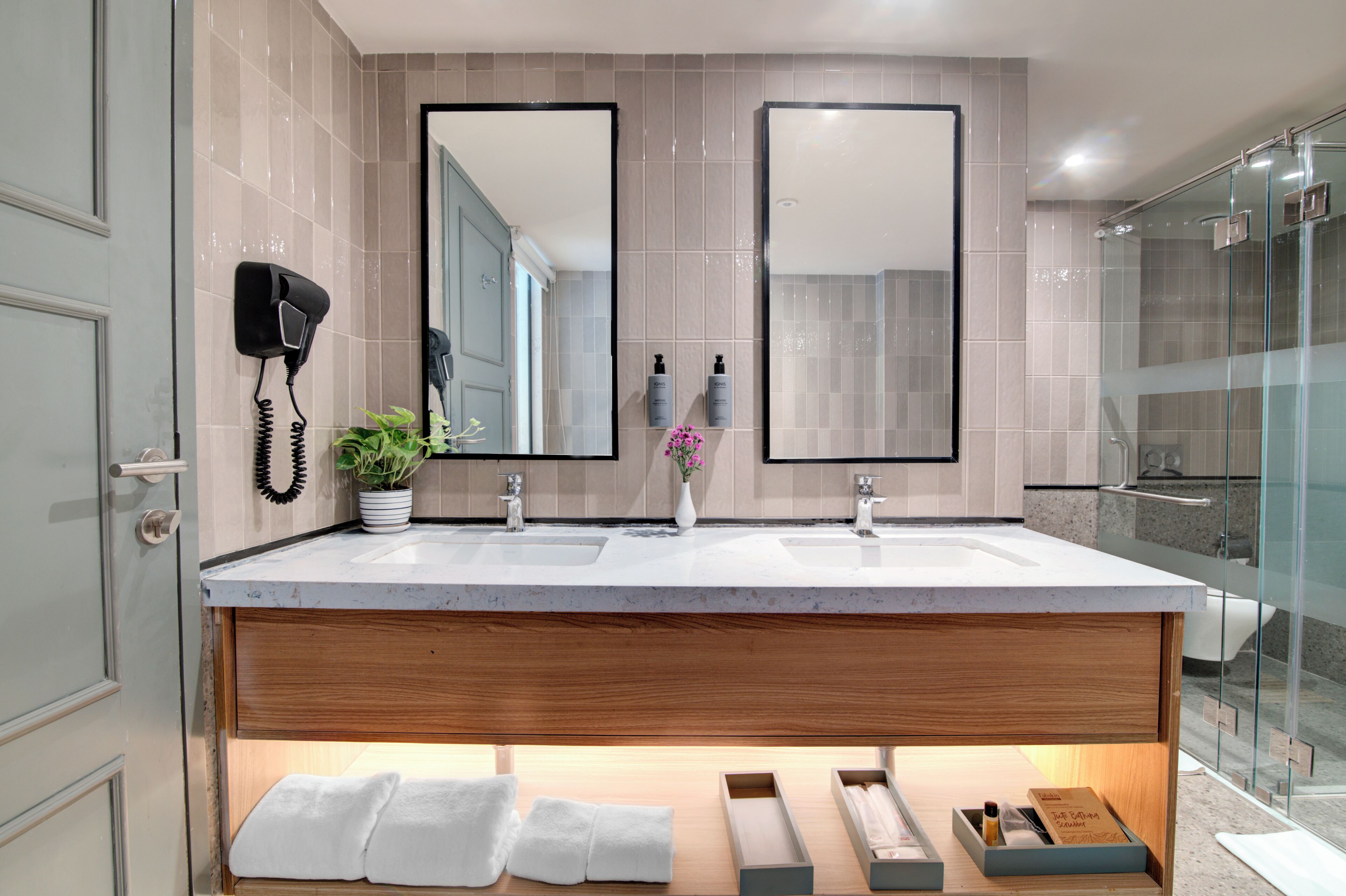 A modern bathroom with two sinks, a hairdryer, a potted plant, and a shower area.
